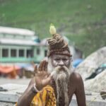 A holy man at Kedarnath Temple offers blessings with a serene background of mountains.